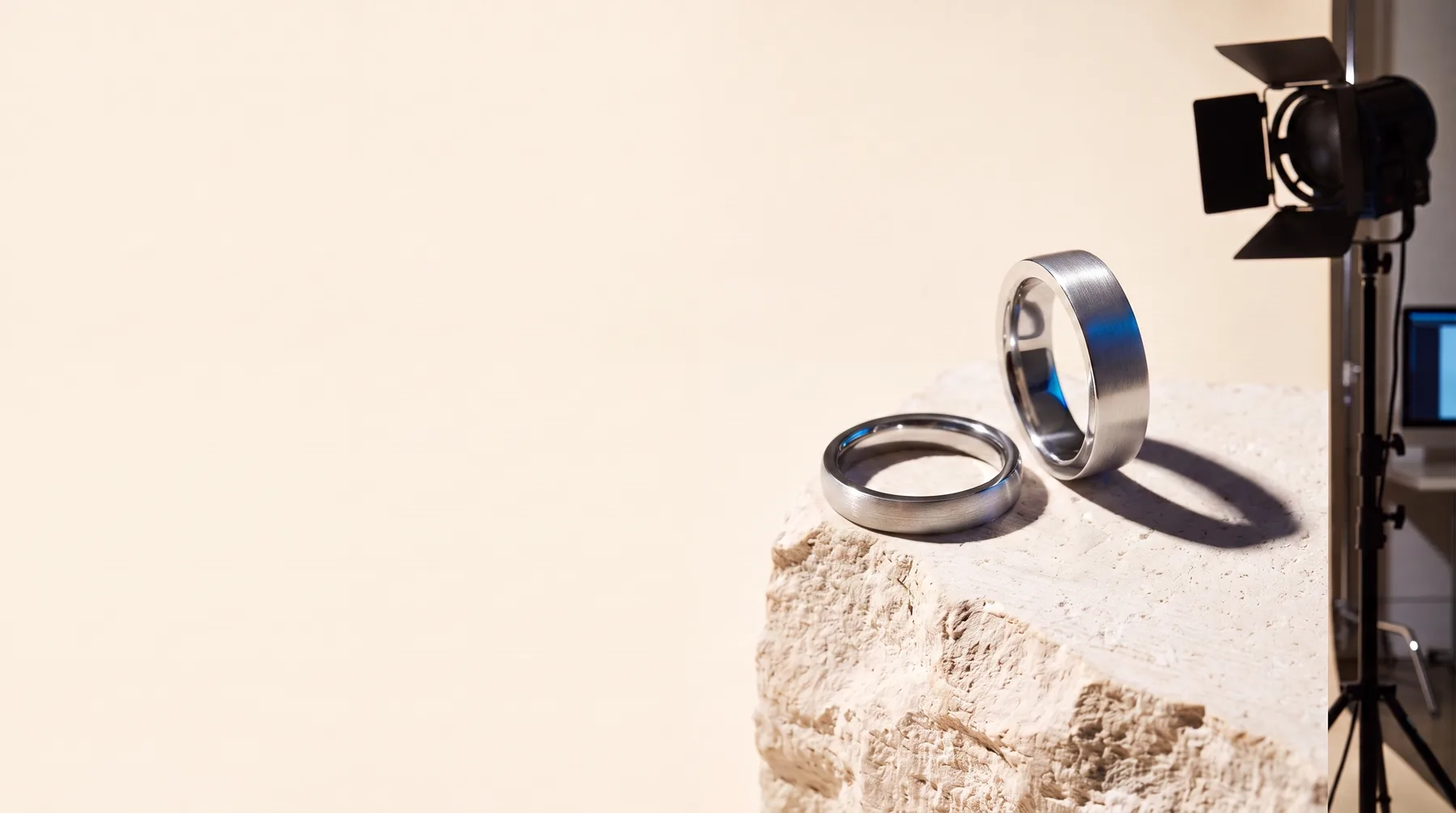 Two modern brushed platinum wedding bands arranged geometrically on a pale limestone slab.