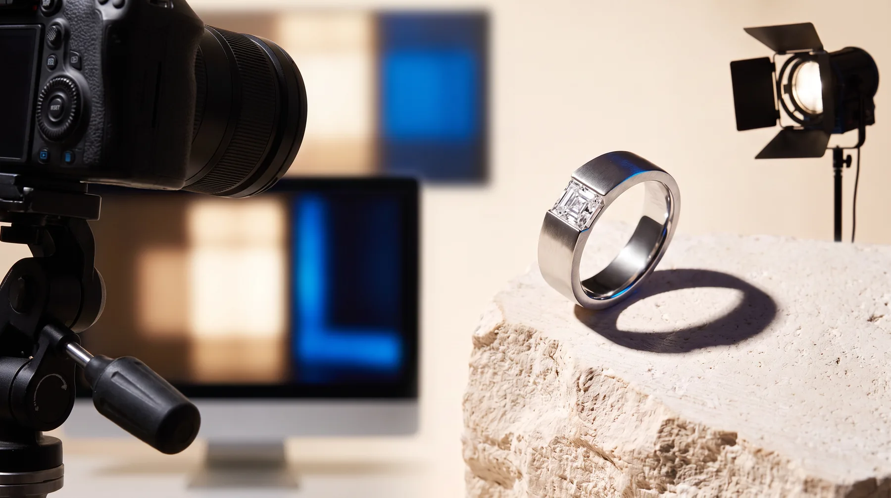 A jewellery photography setup: a camera on a tripod aimed at a ring on a limestone riser, with a studio light and a monitor behind.